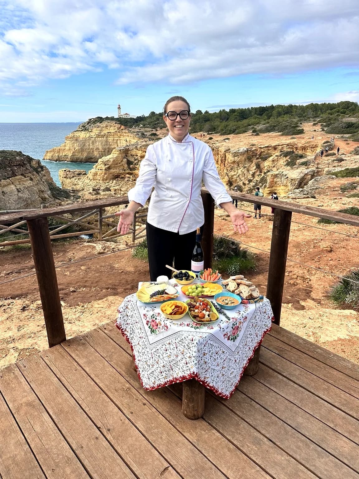Chef Margarida Vargues beside a table of Algarve dishes on a clifftop deck above the sea